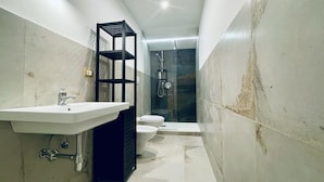 A compact bathroom with a white sink, a black shelf, a toilet, and a shower area. - Nautilus B & B  (Scalea)