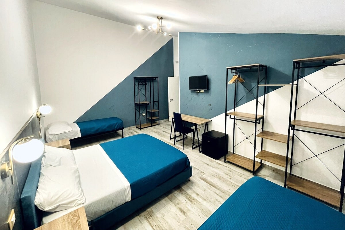 A dormitory room with bunk beds, a desk, a chair, a TV, and a staircase.