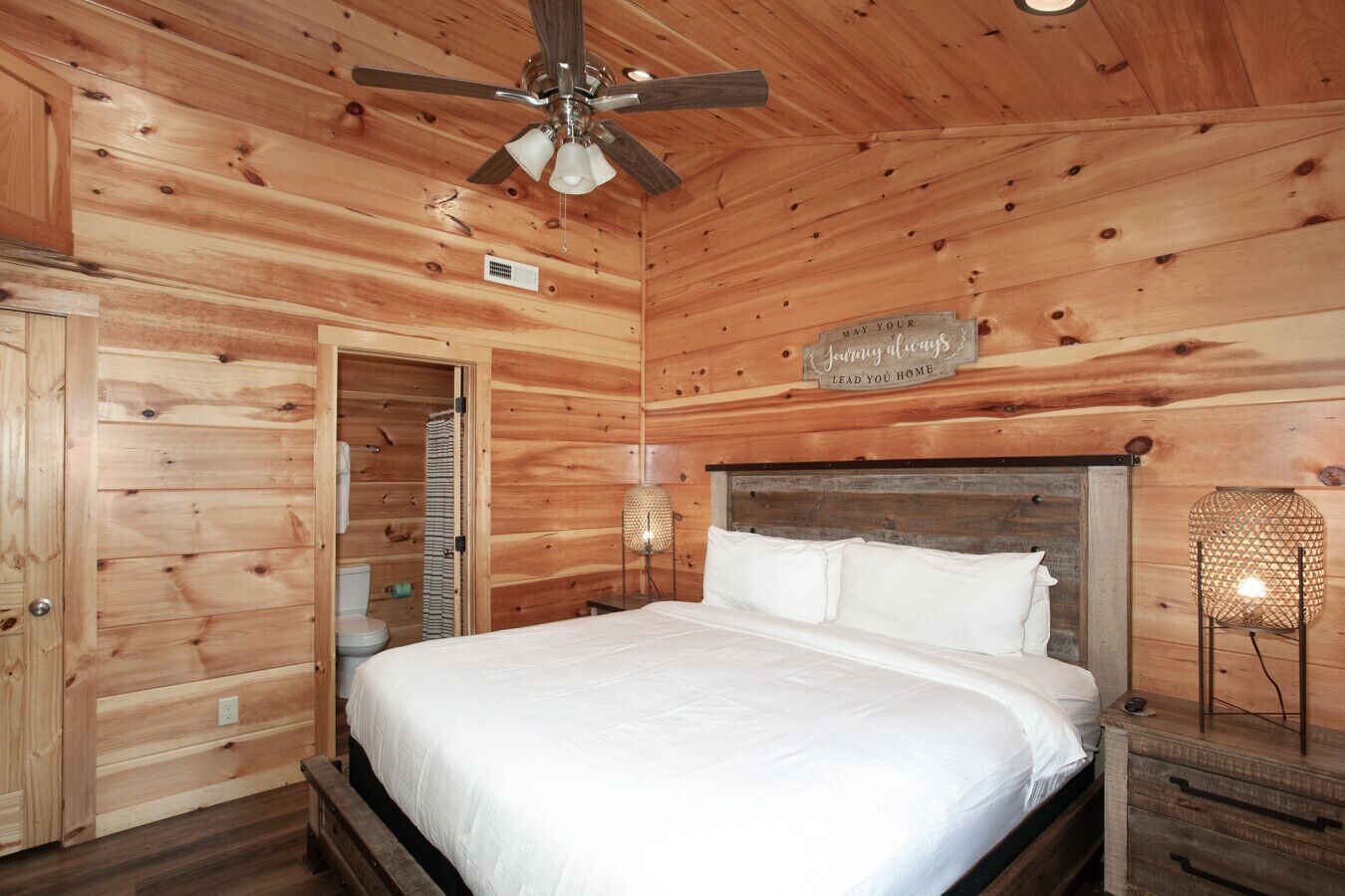 Ein Schlafzimmer in einer Holzhütte mit einem Bett, einem Deckenventilator und einem Nachttisch mit Lampe.