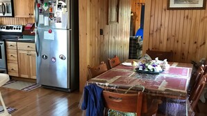Une cuisine aux murs lambrés, dotée d’un réfrigérateur en acier inoxydable, de meubles de rangement en bois et d’une table à manger avec des chaises.
