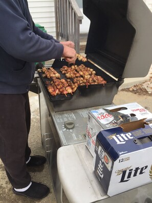 Eine Person grillt Fleischspieße auf einem Grill im Freien, nebenbei steht eine Kiste Miller Lite Bier.