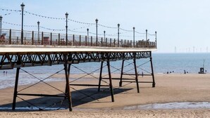 A pier with a metal framework and a flat top, extending over a sandy beach with the sea in the background. - Cozy Caravan , Free Wifi, Pet Friendly (Skegness)