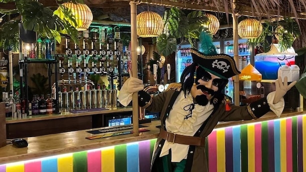 A person in pirate costume at a bar with a colorful striped counter and a thatched roof. - Cozy Caravan , Free Wifi, Pet Friendly (Skegness)