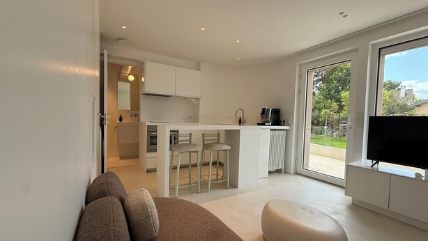 Een moderne keuken met witte kasten, een eethoek met twee stoelen, en een groot raam met uitzicht op groen.