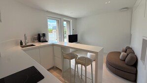 Een moderne keuken met een inbouwvaatwasser, een eethoek met een witte tafel en stoelen, en een gezellige zithoek met een bruine bank.