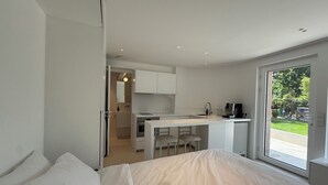 Een moderne slaapkamer met een groot bed, een kleine kitchenette en een schuifdeur naar een balkon.