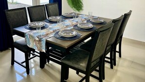 A dining area with a table set for four, surrounded by chairs, with a view of the outdoors through a window.