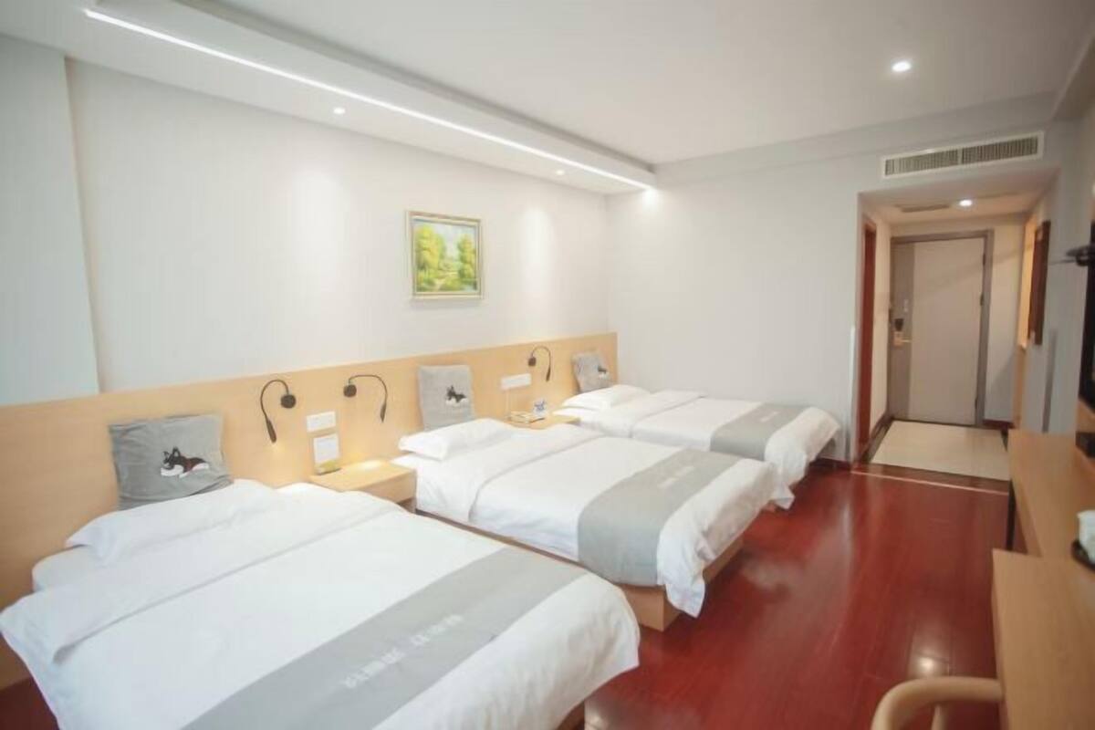A hotel room with three beds, a desk, and a chair. There is a painting on the wall and a door leading to another room.