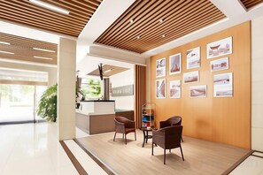 A reception area with a wooden reception desk, a plant, and framed pictures on the wall. - Rujia Pebble Hotel (Baoying Anyi East Road, Baoying Yangzhou) (Baoying)