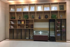 A reception area with a display of framed certificates, a glass display case, and a bookcase with books. - Rujia Pebble Hotel (Baoying Anyi East Road, Baoying Yangzhou) (Baoying)