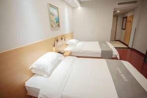 Une chambre d’hôtel avec deux lits, chacun agrémenté de linge de lit blanc et d’un élément décoratif gris. Un tableau est accroché au mur au-dessus des lits, et un porte-manteau se trouve dans un coin de la pièce.