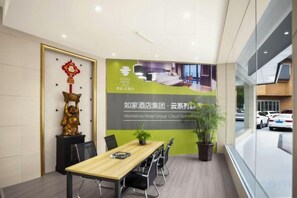 A conference room with a wooden table, chairs, a potted plant, and a large poster on the wall. - Rujia Pebble Hotel (Baoying Anyi East Road, Baoying Yangzhou) (Baoying)