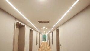 A long, narrow hotel corridor with a patterned carpet, recessed lighting, and doors on both sides.