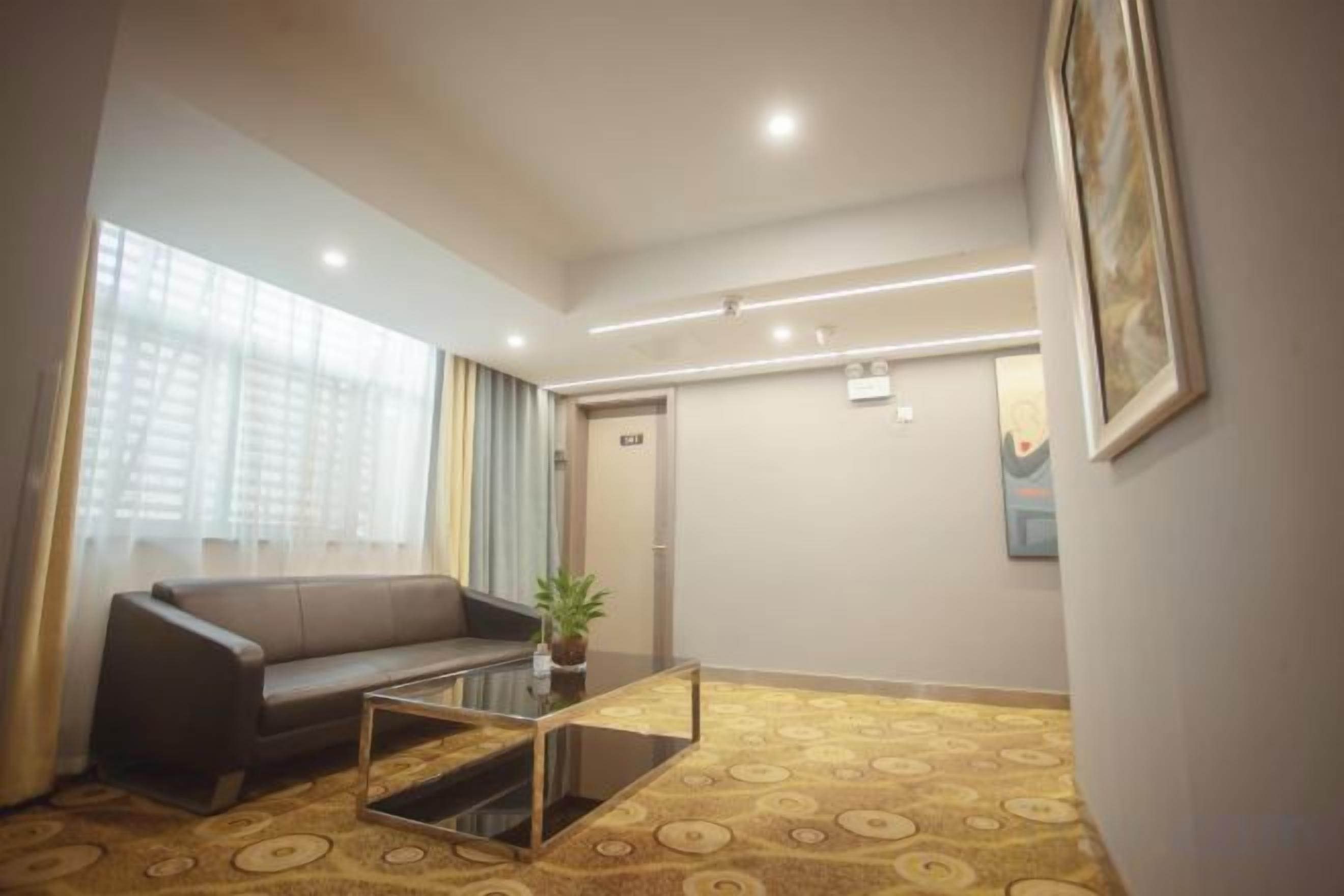 A hotel room with a sofa, a coffee table, a potted plant, and a patterned carpet.