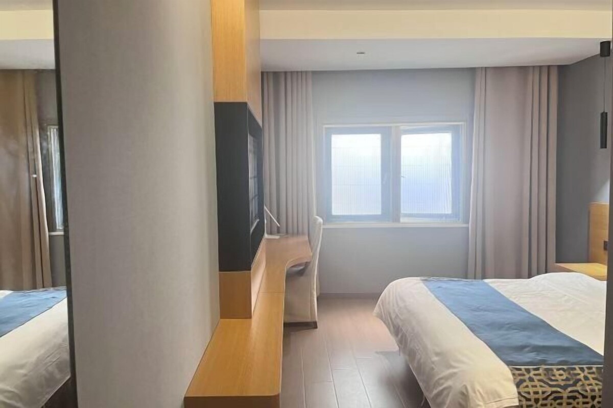Une chambre d’hôtel avec deux lits, un bureau et une fenêtre avec des rideaux.