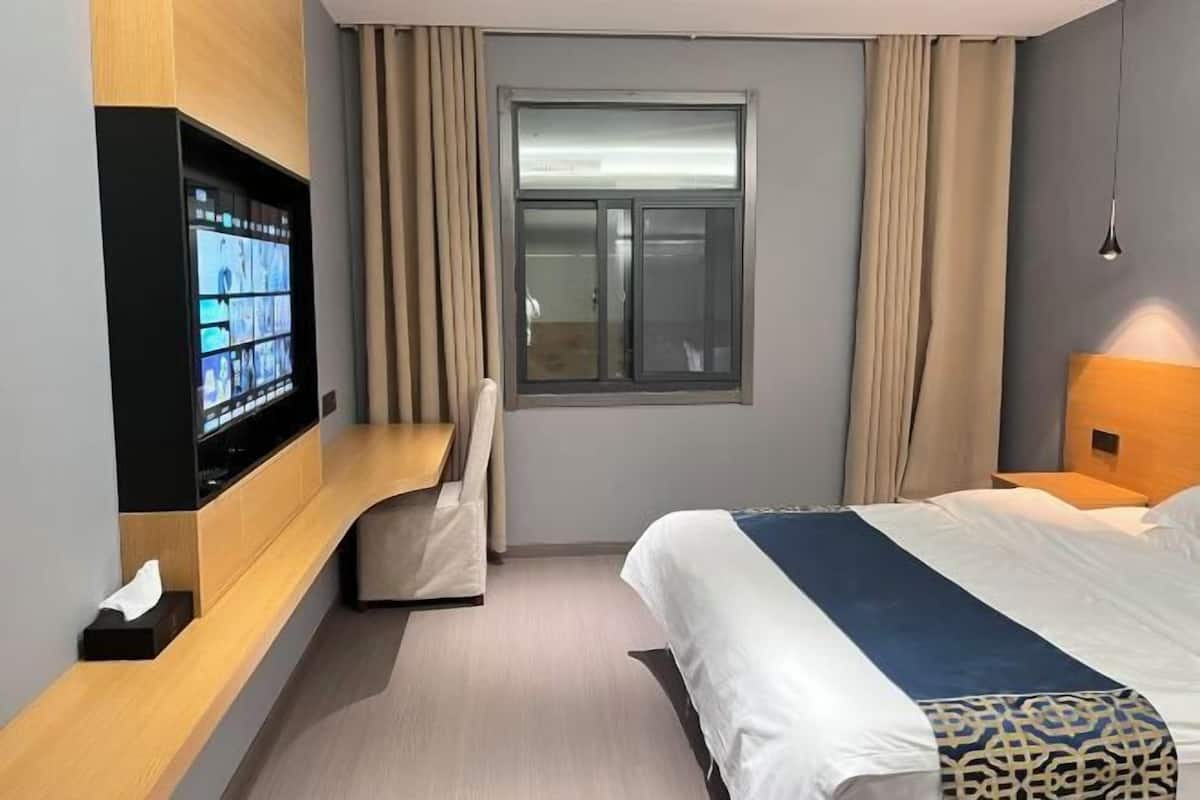 A hotel room with a bed, a TV mounted on the wall, a window with curtains, and a bedside table.