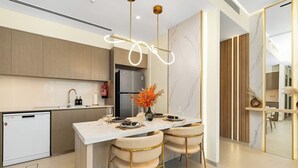 Een moderne keuken met een centraal eiland, roestvrijstalen apparatuur en een eetgedeelte met een marmeren aanrechtblad en gouden stoelen.
