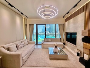 A modern living room with a sofa, a coffee table, and a TV. There is a large window with a view of a cityscape.
