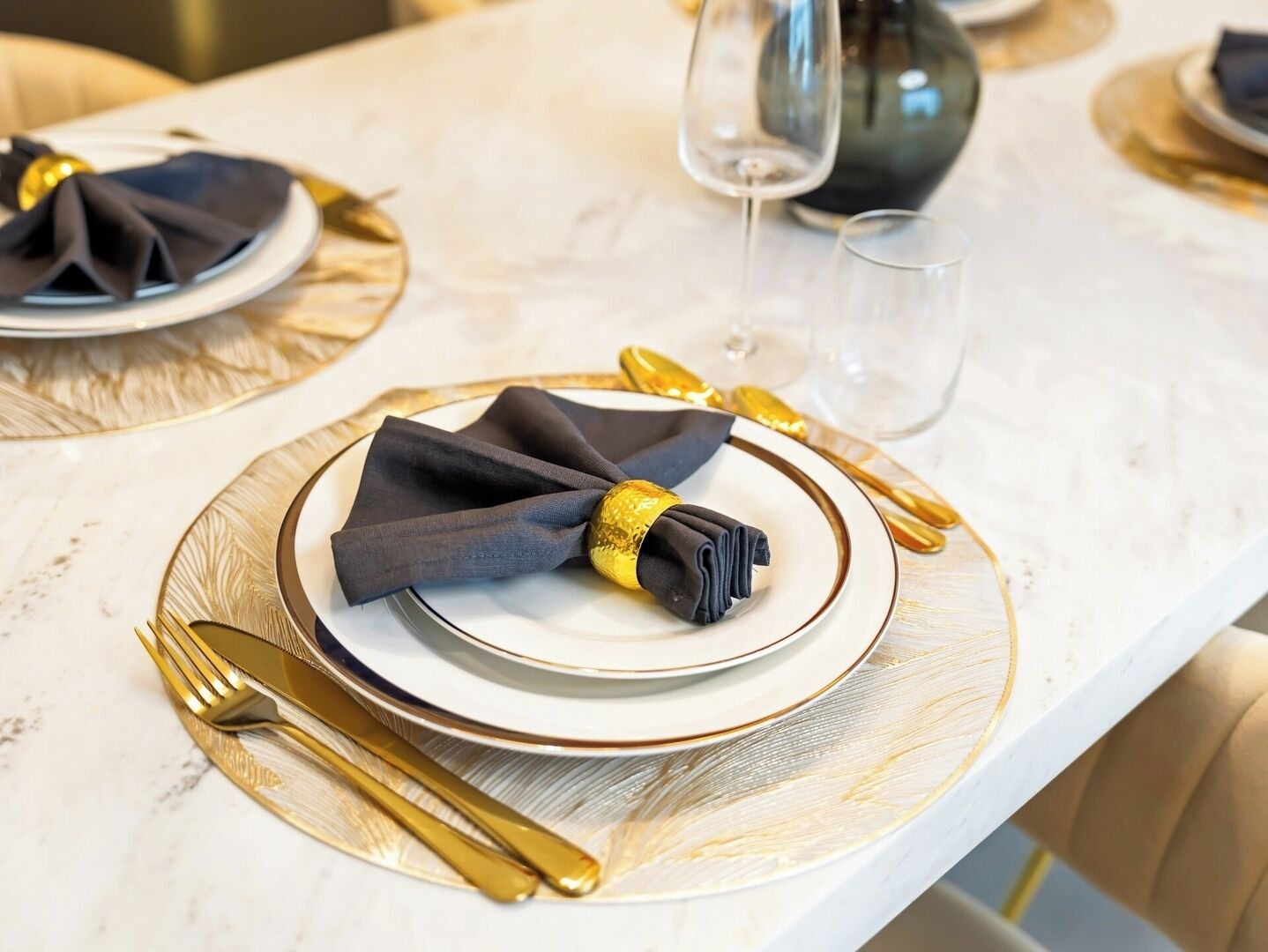 Une table dressée avec une serviette pliée, une assiette, un verre et des couverts dorés.