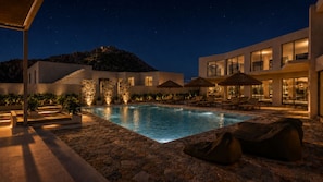 A modern pool area with stone flooring, lounge chairs, and umbrellas.