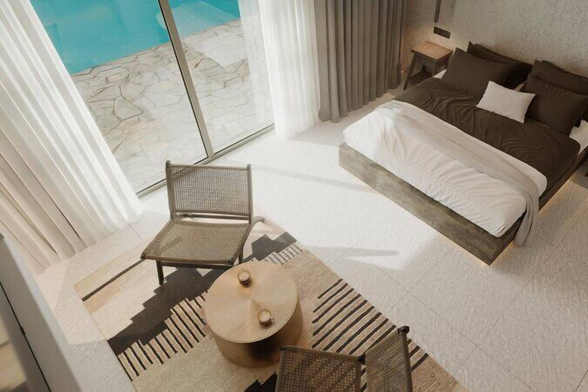 Een moderne hotelkamer met een groot bed, een zithoek met een stoel en een klein tafeltje, en uitzicht op een zwembad.