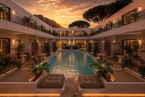 A modern hotel with a central pool, outdoor seating, and a sunset view.