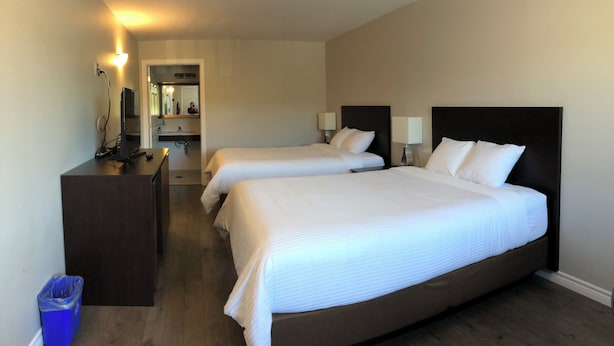 A hotel room with two beds, a desk, a mirror, and a trash bin. - Kow's Inn (Bras D'or)