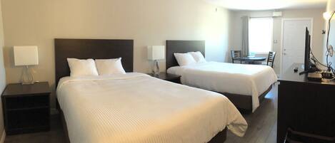 A hotel room with two beds, a desk, a chair, and a small table.
