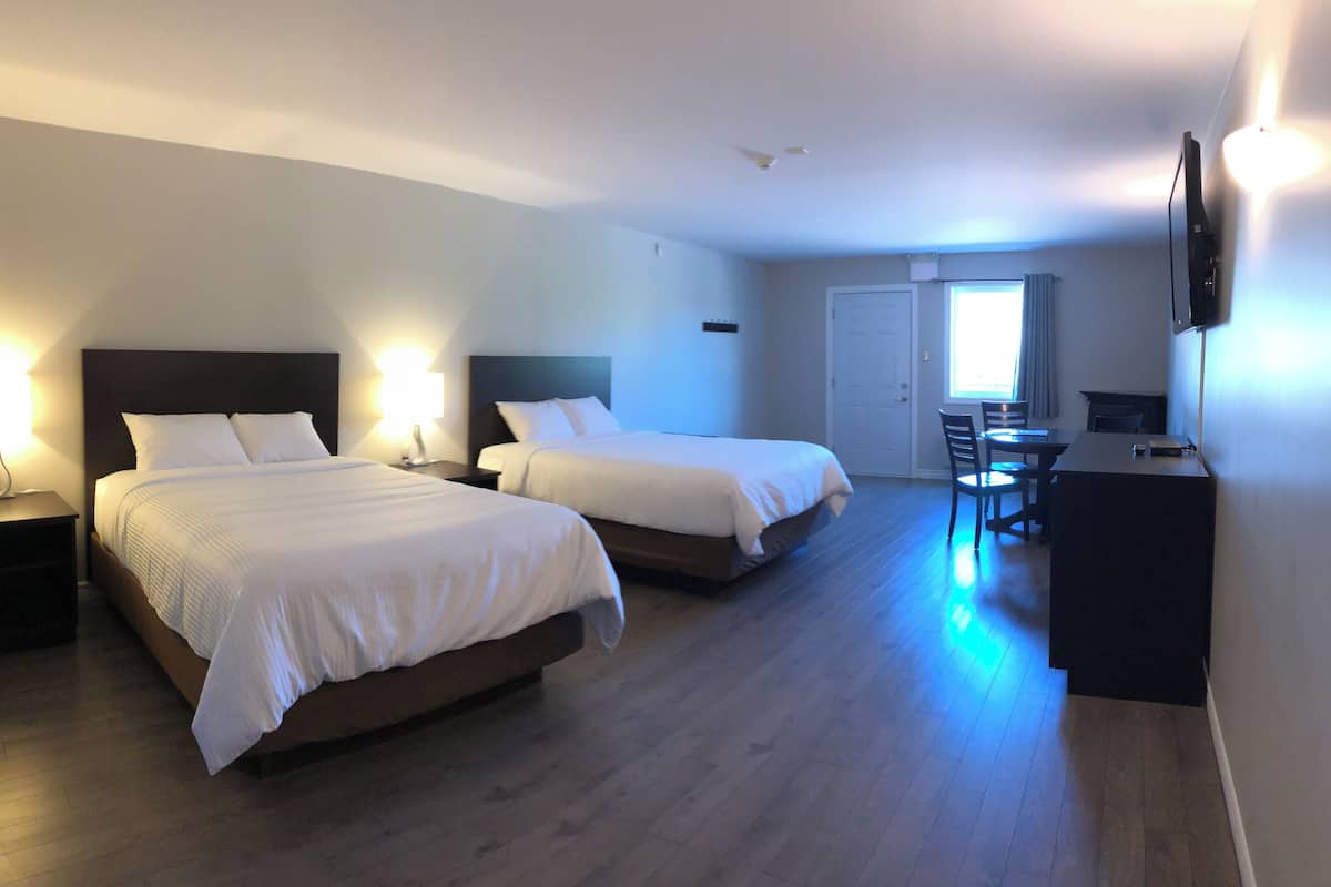 A hotel room with two beds, a desk, a chair, and a TV mounted on the wall.
