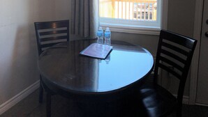 A small dining area with a round table and two chairs, a window with a view of a deck and trees, and a bottle of water on the table. - Kow's Inn (Bras D'or)