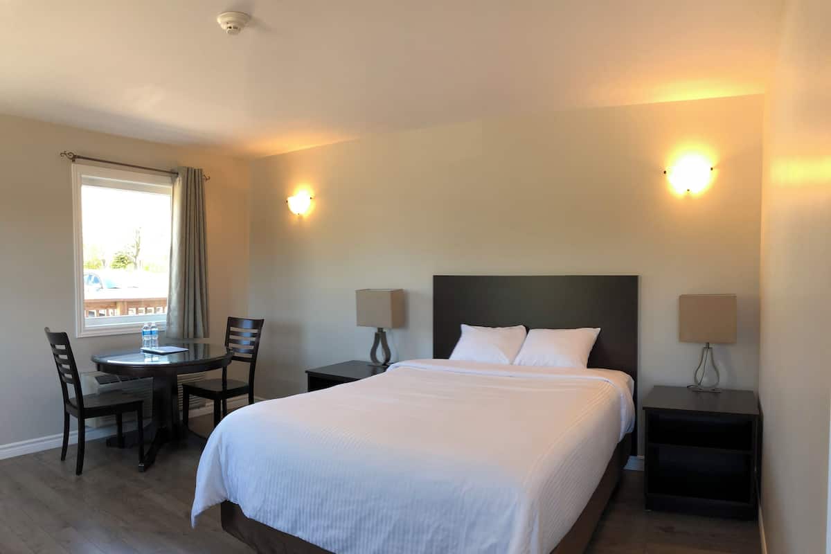 A hotel room with a large bed, two bedside tables with lamps, a small table with chairs, and a window with curtains.