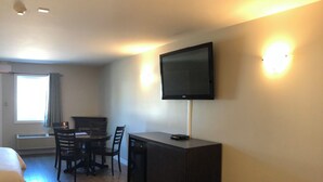 A hotel room with a flat-screen TV mounted on the wall, a dining table with chairs, a small cabinet, and a bed. - Kow's Inn (Bras D'or)