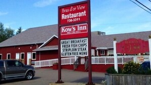 A restaurant signboard with 'Bras d'Or View Restaurant' and 'Kow's Inn' names, along with a list of breakfast items like fresh fish, chips, steak, and a gluten-free menu. - Kow's Inn (Bras D'or)