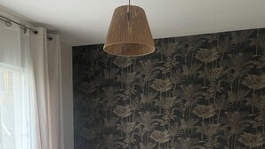 Een slaapkamer met een bed, een hanglamp, een nachtkastje en een raam met gordijnen.