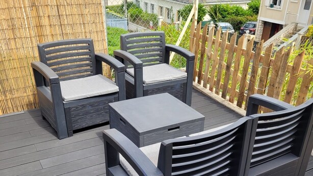 Een terras buiten met donkere meubels, waaronder twee stoelen en een tafel.