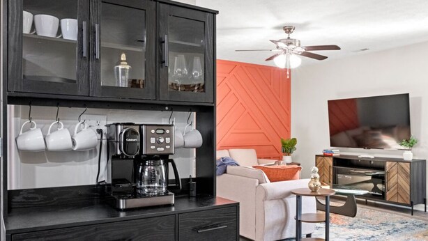 A modern kitchen with a coffee maker, cabinets, and a dining area with a table and chairs.