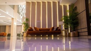A modern lobby with a reflective floor, a brown sofa, and vertical wooden panels. - Grand Season 3 (Al Khobar)