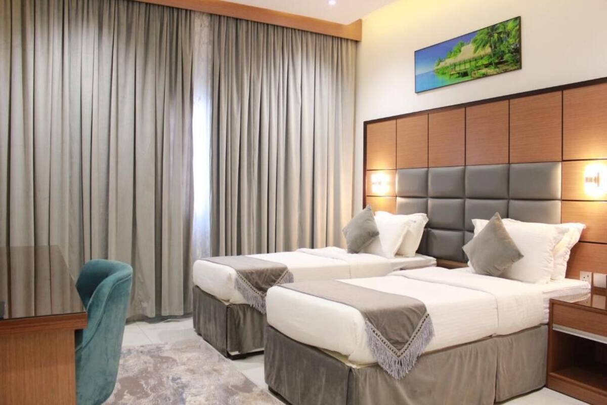 A hotel room with two beds, a large window with curtains, a wooden headboard, and a painting on the wall.