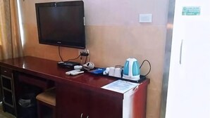 Una habitación de hotel con un escritorio de madera, un televisor de pantalla plana, una tetera y un pequeño cubo de basura.