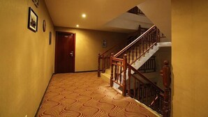Un pasillo con alfombra estampada, puertas de madera y una escalera con barandillas de madera.