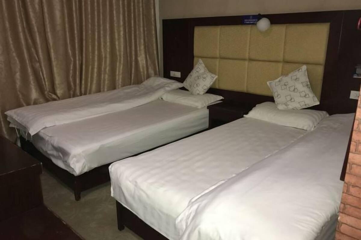 Quarto de hotel com duas camas de solteiro, cada uma com cabeceira e almofadas.