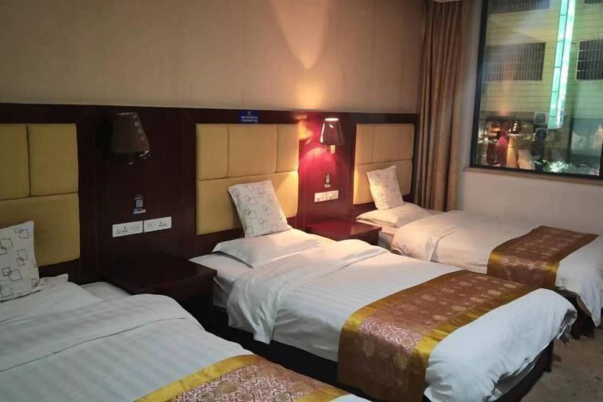 Quarto de hotel com três camas de solteiro, cada uma com cabeceira e mesas de cabeceira. Há uma janela com vista para o exterior.