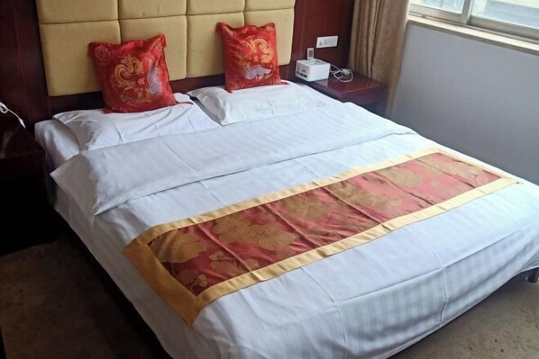 A neatly made bed with white and red bedding, a headboard, and a bedside table with a lamp.