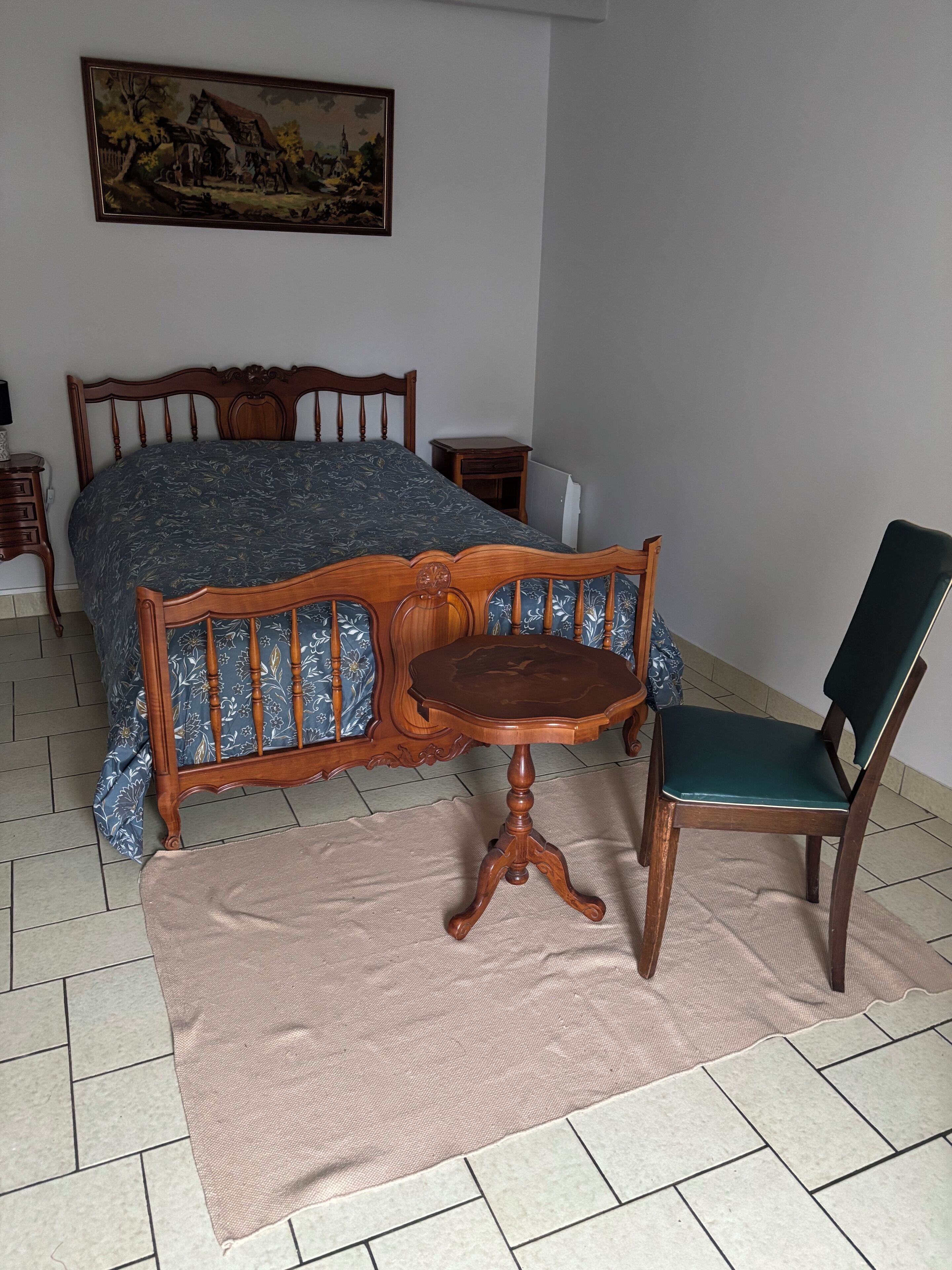 Une chambre à coucher avec un lit, une chaise en bois, une petite table et un tableau accroché au mur.