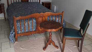 Une chambre à coucher avec un lit, une chaise en bois, une petite table et un tableau accroché au mur.