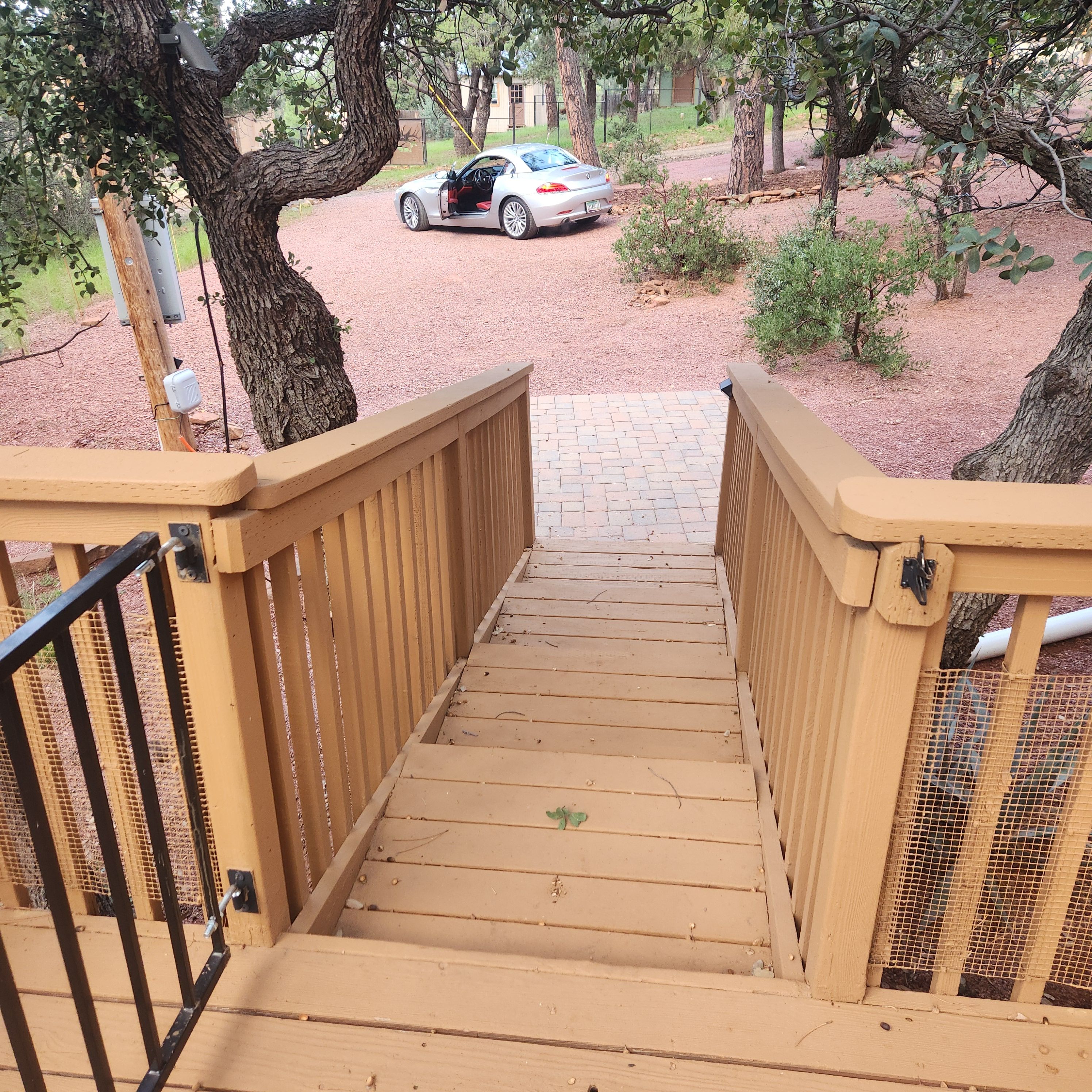 A wooden staircase leading to a paved area with a parked car in the background.
