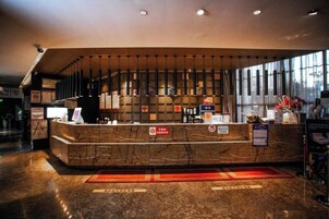 Una zona de recepción de hotel con un mostrador de mármol, un ventanal grande y una alfombra roja.