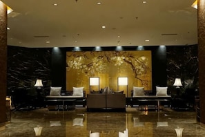 A lobby with a marble floor, two sofas with lamps, and a wall with a tree mural.