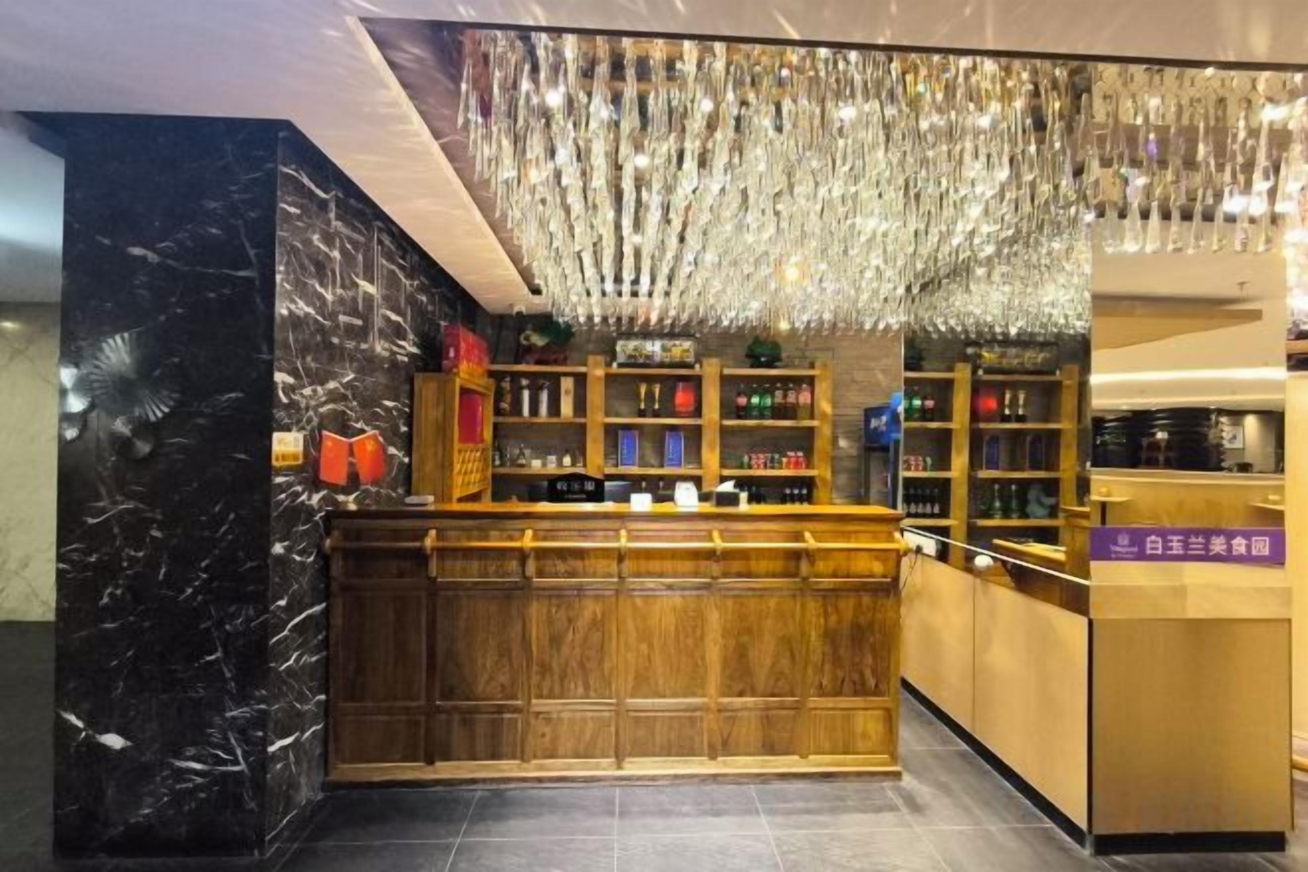 A bar area with a wooden counter, shelves with bottles, and a hanging light fixture.
