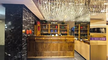 A bar area with a wooden counter, shelves with bottles, and a hanging light fixture.